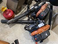Two backpack blowers with tubes and padded straps laid on garage floor