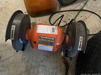 Front and side view of an orange Central Machinery 8" bench grinder with grinding wheels and protective guards.