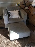 Overall view of gray armchair with ottoman and white tassel pillow