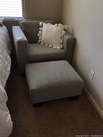 Grey fabric rectangular ottoman placed in front of matching armchair in bedroom corner