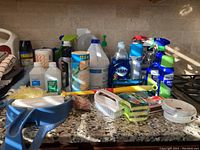 Photo showing various cleaning bottles, sponges, towels, and dustpan on kitchen counter.