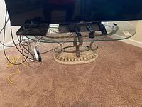 View showing full glass oval top and the iron scroll supports connecting to the stone-like base, with some electronics on top indicating size.