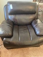 Front view of dark brown faux leather electric recliner chair showing cushioned armrests, padded backrest, and seat.