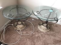 Pair of round glass topped end tables sitting on carpet, showing full top and frame detail.