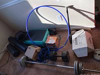 Photo of exercise equipment lot showing barbell with metal weights, foam rollers, aerobic step platform, hula hoop, resistance bands, dumbbell and boxes
