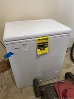 Closed white Hotpoint chest freezer on a concrete floor with EnergyGuide sticker on front.