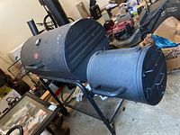 Photo of full Char-Griller barrel smoker and grill combo unit with side firebox, set in garage among other items.