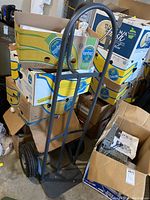 Hand truck positioned vertically loaded with empty cardboard boxes inside a garage, showing front and side views.