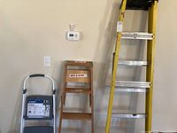 Cosco 2-step folding stepstool next to wooden ladder and yellow fiberglass ladder.