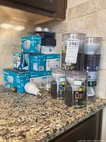 Wide view of the lot showing stacked boxes of Ecosmart LED light bulbs on a kitchen counter with other items including cylindrical Reveal LED dimmable bulbs and accessories.