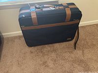 Full view of Samsonite black and brown suitcase standing upright on carpet under a window