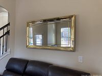 Mirror hung on wall above black leather sofa, showing full item in a living room setting.