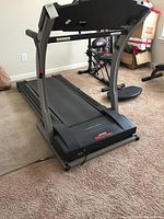 Full view of black Pro-Form treadmill on carpet showing running belt and front wheels for transport.