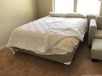 Full view of queen size bed with white quilted comforter, white fitted sheet, and white pillow.
