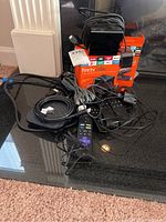 Photo showing Amazon Fire TV Cube with packaging box, remotes, and charging cables on black surface.