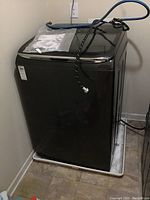 Full view of the top load washer in laundry area on protective tray with hoses attached