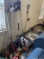 Three Stihl trimmers leaning against wall alongside pruning attachments and red trimmer line spool