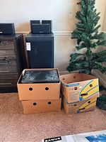 Overall view of boxed stereo components and speakers arranged by a wall and artificial Christmas tree.