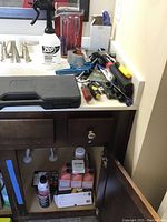 Tools, sprayer, duct tape and screwdrivers arranged on bathroom sink counter and under sink cabinet area.