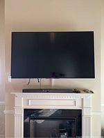 Front view of mounted TV above fireplace mantel showing soundbar and remotes