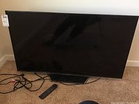 Full front view of the TCL 48-inch flat-screen TV on carpet with cables and remote.
