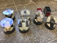 Six watches in display cases on tile floor, including a gold-tone watch, black watch with jewel tones, and watches with protective plastic covers
