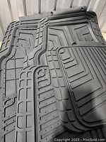 Four black rubber all-season car floor mats stacked showing textured and grooved surfaces.