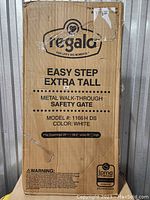 Full view of the Regalo Extra Tall Baby Gate cardboard box, showing brand, model, size, and warnings.