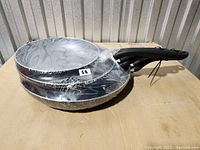 Set of three frying pans stacked by size, wrapped in clear plastic.