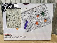 Photo of the granite cutting board packaging showing the product and some items on top of it, illustrating its use.