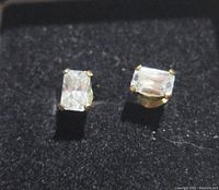 Pair of rectangular radiant cut clear cubic zirconia stones set in 14k gold filled prong stud earrings shown on black fabric background in a box.