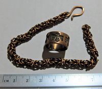 Copper bracelet alongside a copper ring with black engraved designs on a white background with a centimeter ruler for scale. Bracelet is thick chain link style with hook clasp, approx. 20 cm long.