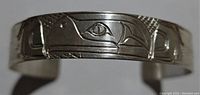 Close-up front view of the silver cuff bracelet showing West Coast Native art design with animal motifs and textured background.