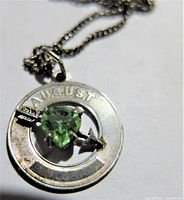Close-up photo of silver round pendant with August birthstone green heart-shaped gemstone and arrow detail