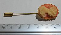 A full-length photo of the cameo stick pin beside a centimeter ruler showing it measures about 6 cm in length.