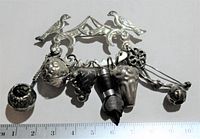 Vintage silver-tone charm brooch pin with bird design and multiple hanging charms, displayed against a white background with a ruler for scale.