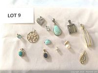 Full laid out photo showing all 13 pendants with variety of colors and shapes including turquoise blue, pearl, clear stones and gold/silver tones.