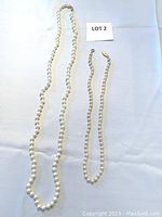 Full view of two knotted pearl necklaces, one longer and one shorter, laid flat on white background.