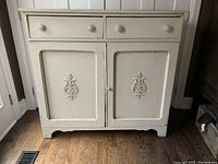 Front view of antique wooden sideboard showing the three drawers above two cabinet doors with carved floral detail and distressed off-white paint finish