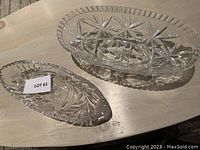 Two clear crystal bowls on wooden surface, one large oval and one smaller oval, showing intricate cut patterns