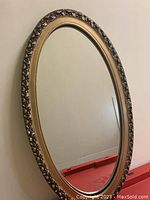 Front view of the oval mirror showing the ornate frame and reflective glass surface.