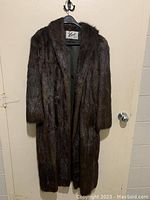Full exterior view of the long brown fur coat on a hanger showing its length and fur texture.