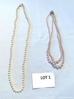 Full view of both pearl necklaces, one single strand white pearls and one double strand smaller pink pearls.