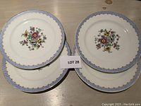 Four Limoges porcelain dessert plates with floral motifs and blue gold rims displayed on a table, one plate with visible chip.
