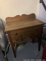 Front view of small oak side table with three drawers and scalloped backboard.