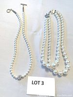 Full view of two pearl necklaces, one single strand and one double strand, displayed flat with toggle clasps visible.