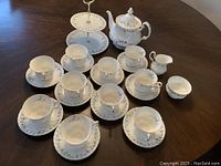 Full set arranged on table showing 10 cups, 10 saucers, teapot, cream, sugar and cake stand