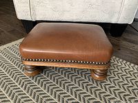 Top and side views showing the brown leather surface, nailhead trim, and wooden legs.