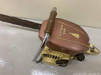 Front-side view of the vintage Pioneer S620 chainsaw showing the reddish-brown top cover with gold lettering and logo, yellow engine body, and brown handle on the metal frame.