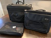 Three black bags including a wheeled business case, laptop bag, and carrying bag displayed on table